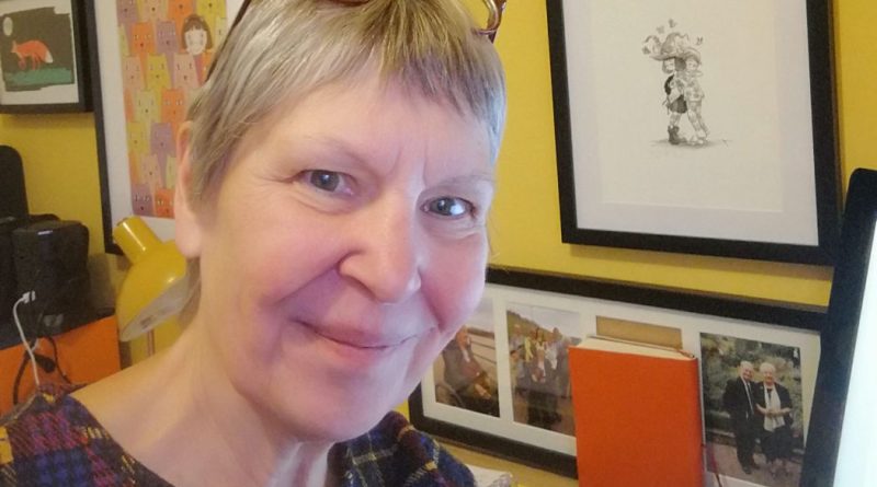 Lady with short grey hair and glasses perched on her head smiling at the camera