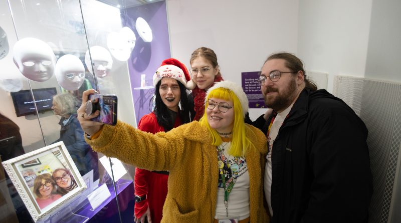 group of 4 people enjoying a museum visit. One person is holding a phone up, and taking a group selfie.