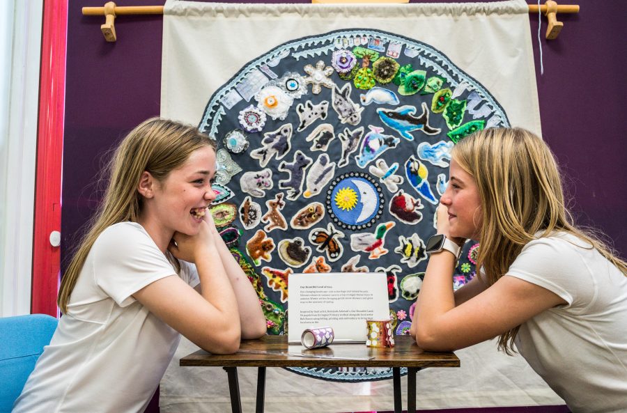 Two girls sit in front of their interpretation of Our Beautiful Land print.